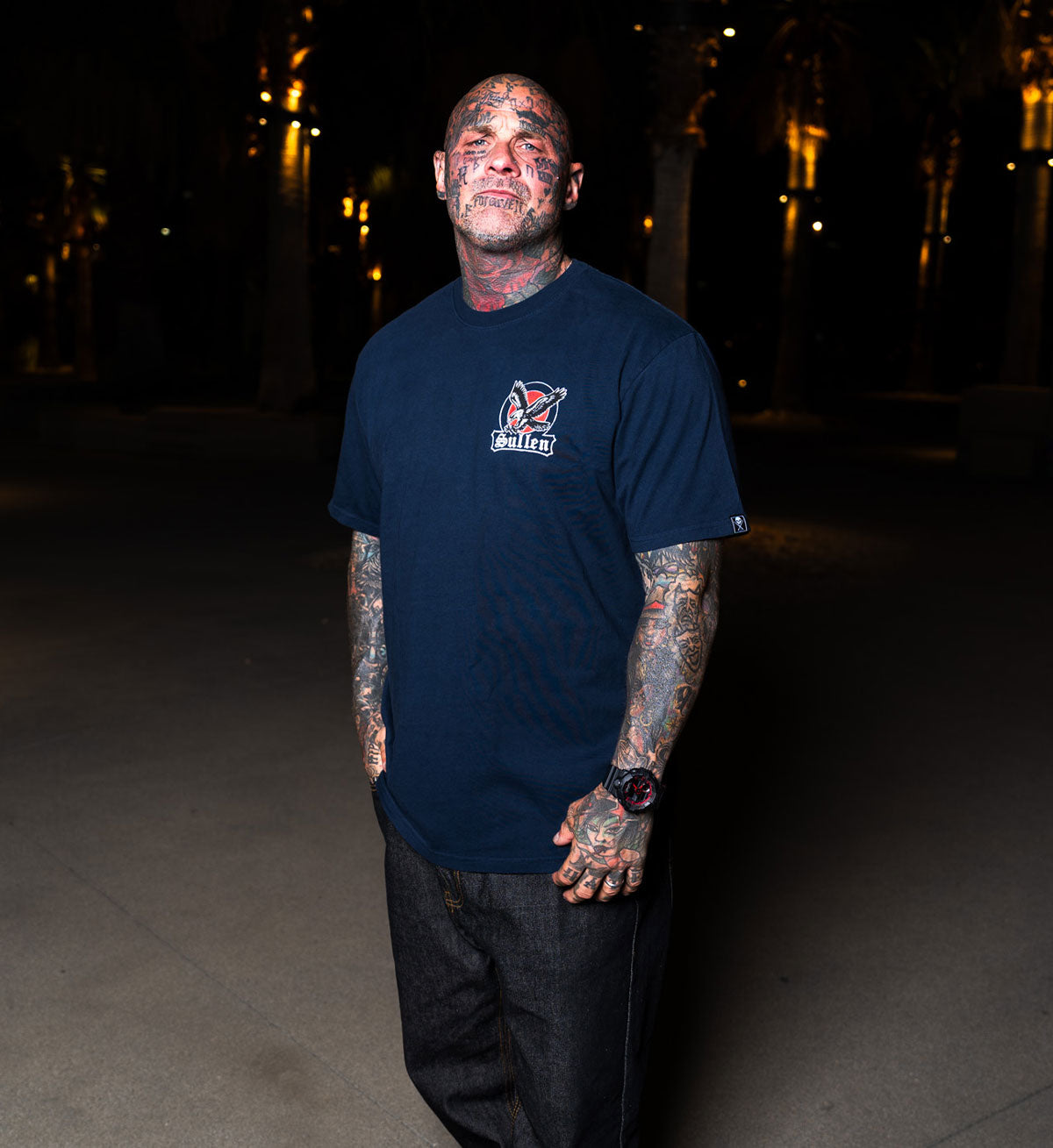 Man wearing a navy blue t-shirt with a logo, standing outdoors at night.