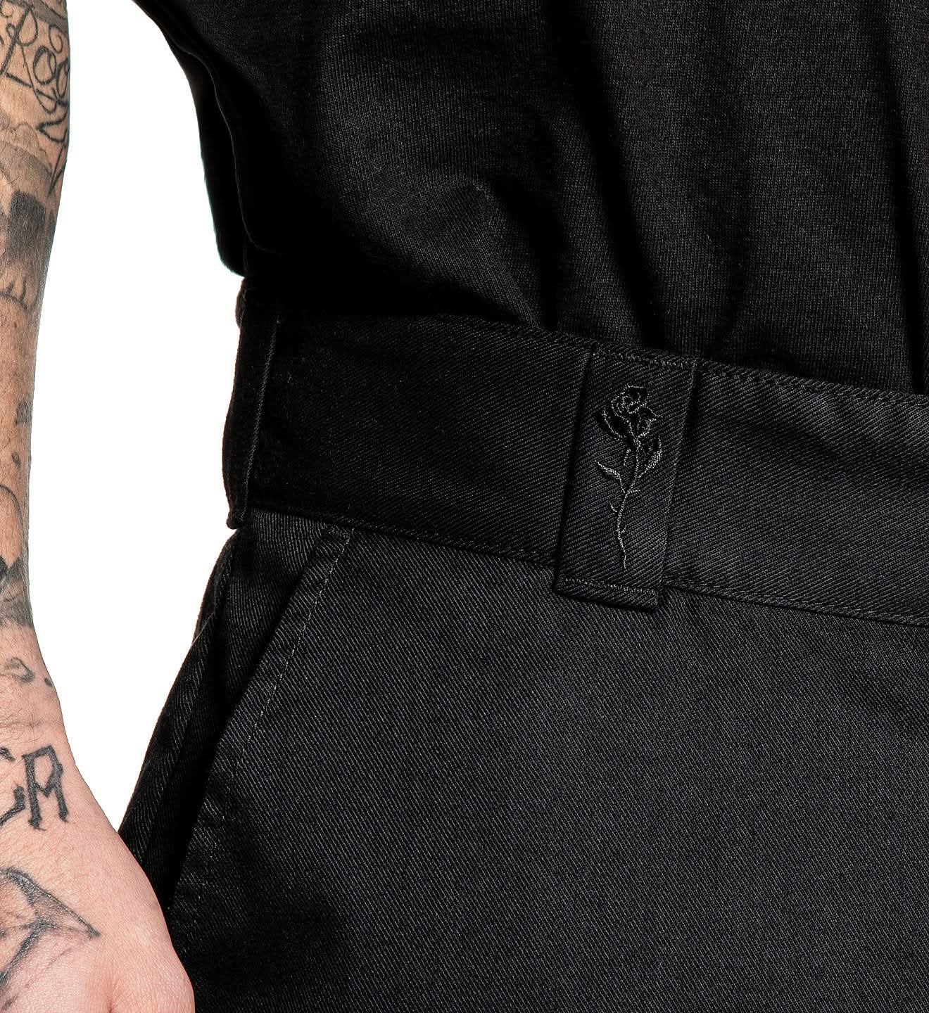 Person wearing black pants with a tattooed arm visible