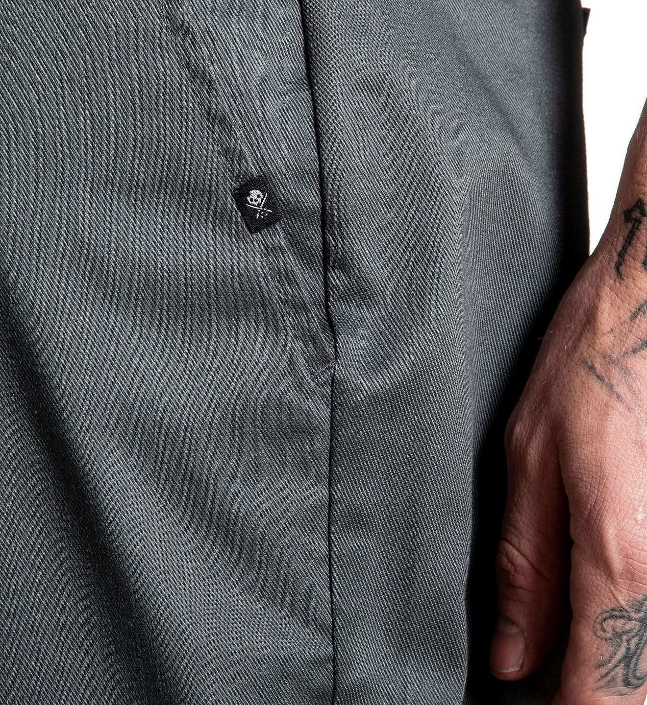 Close-up of a gray shirt with a button and a hand with tattoos on a white background