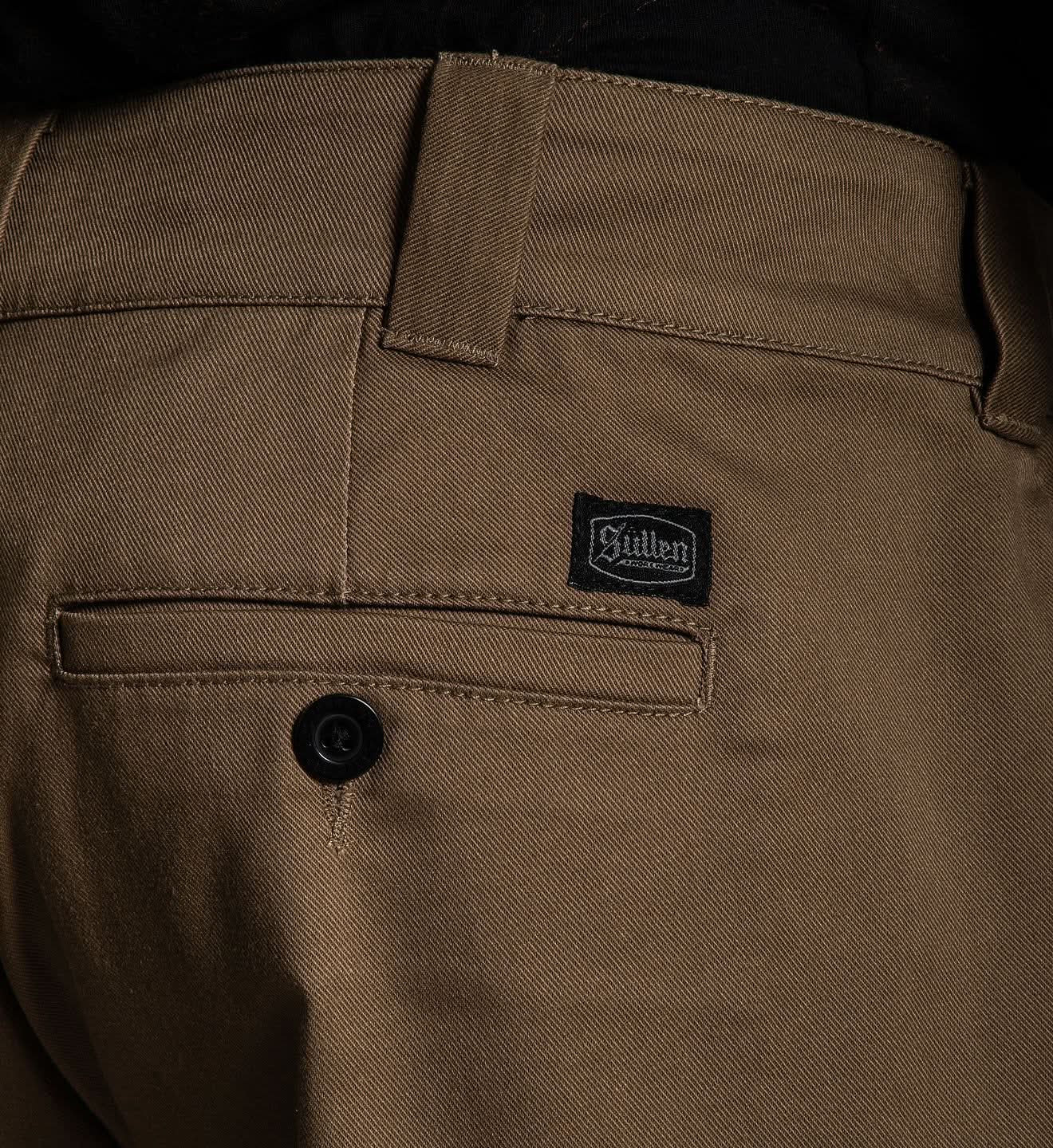 Close-up of brown pants with a brand logo on the pocket.