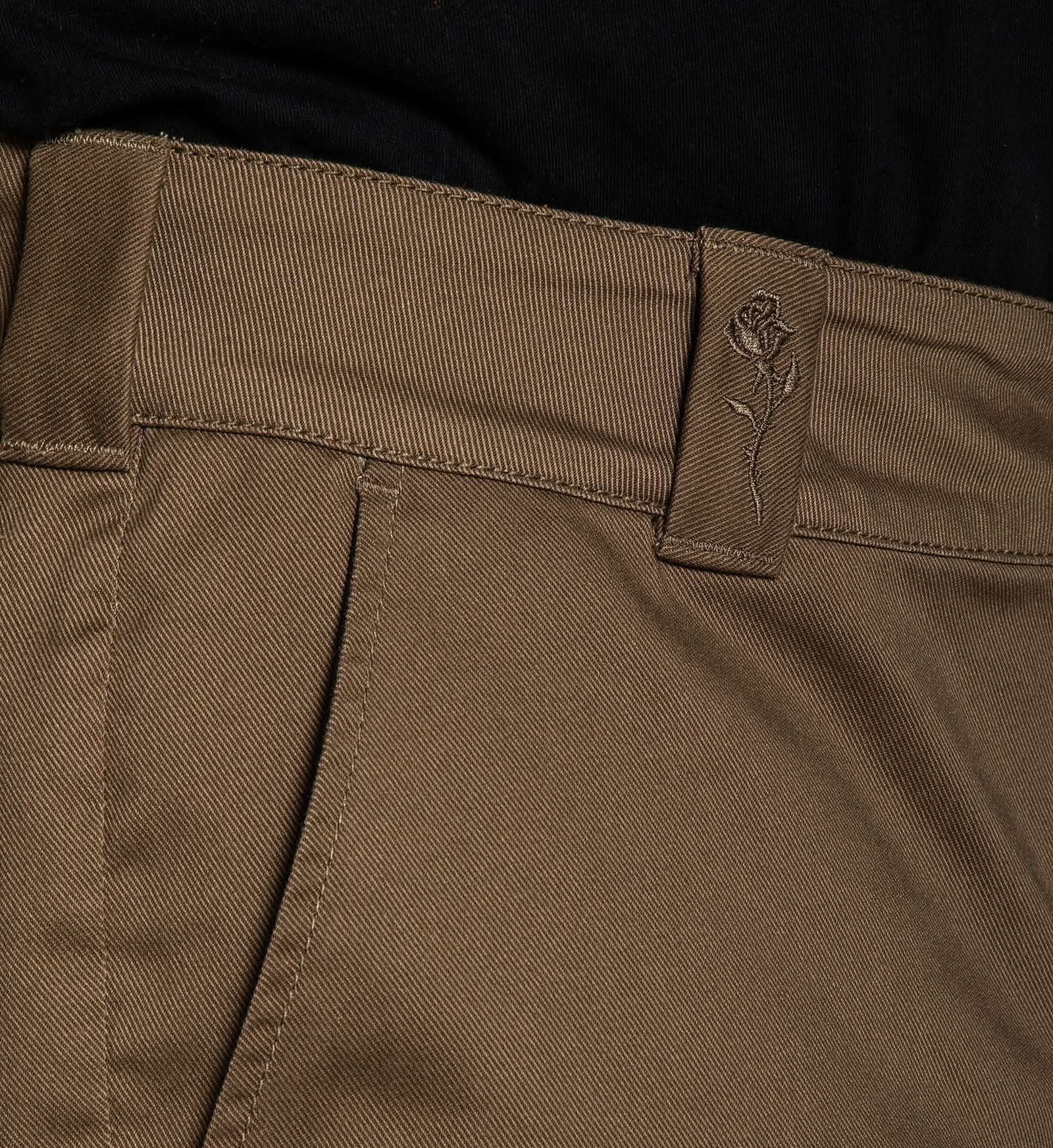 Close-up of brown pants with a brand logo on the pocket corner.