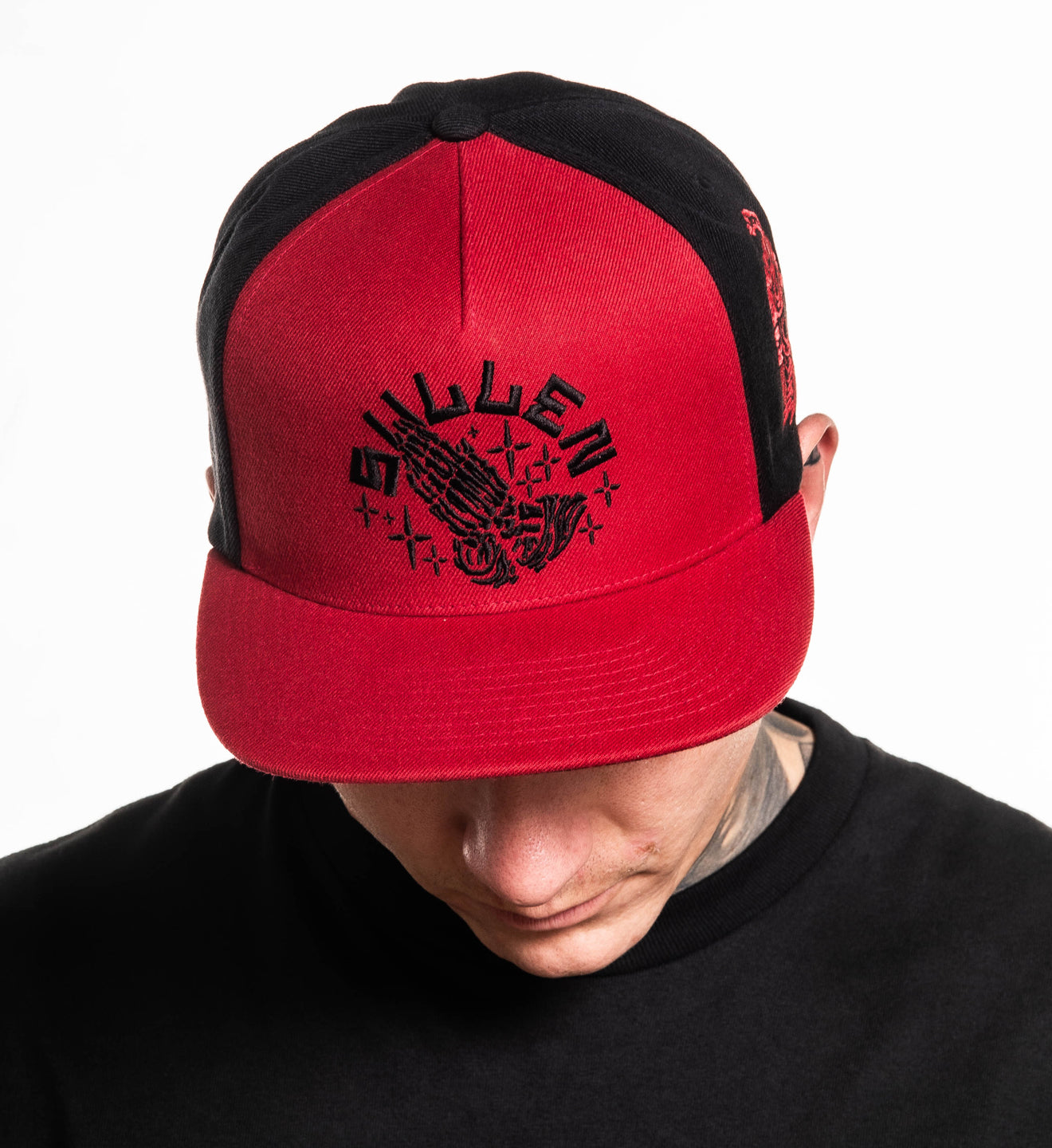 Red and black cap with a logo worn by a person on a white background