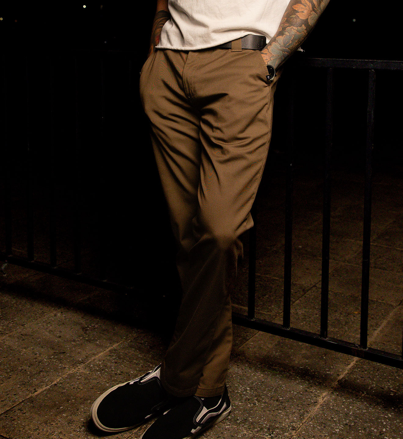 Person wearing brown pants and black shoes standing against a dark background