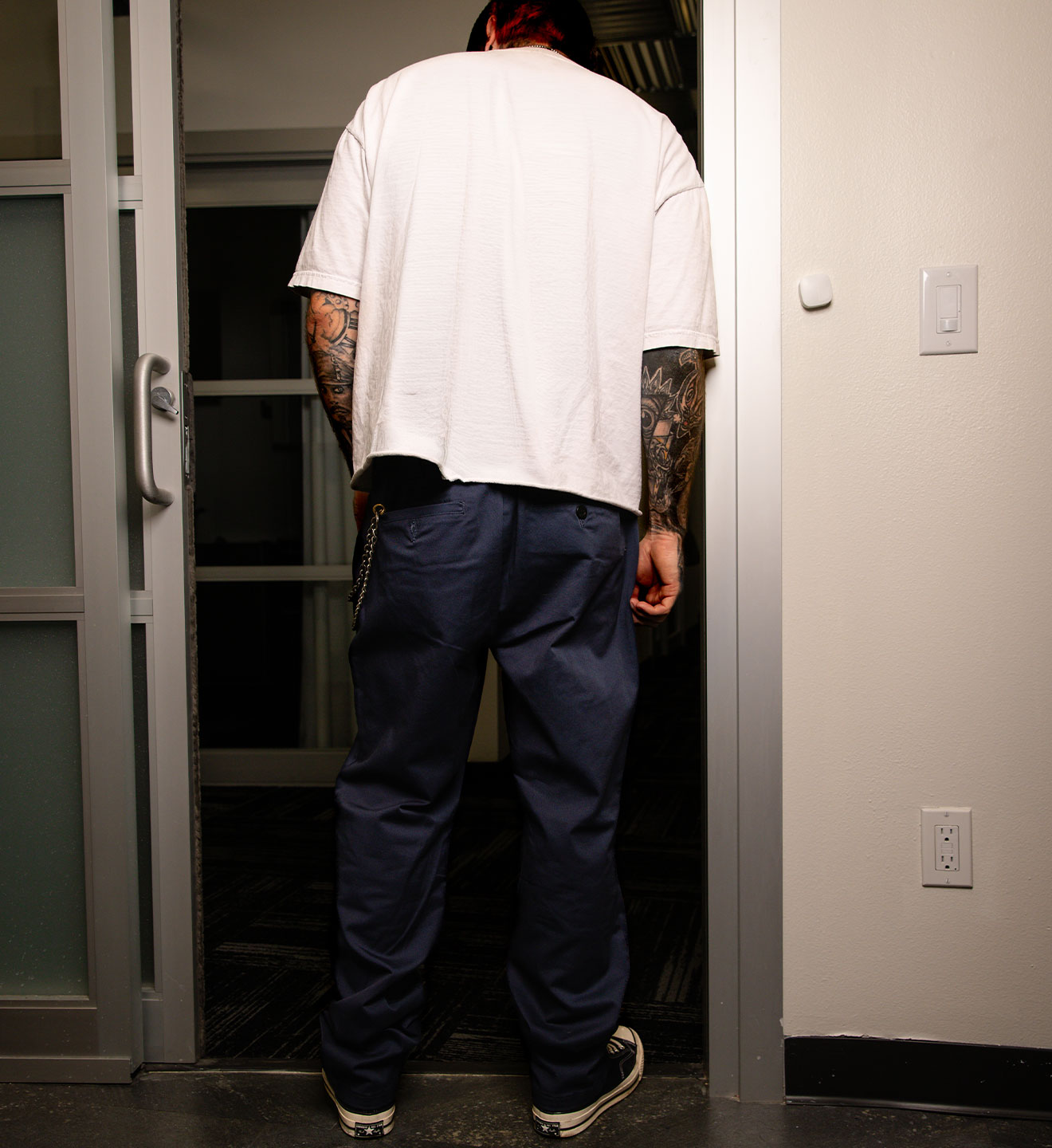 Person wearing a white shirt and blue pants standing in a doorway.