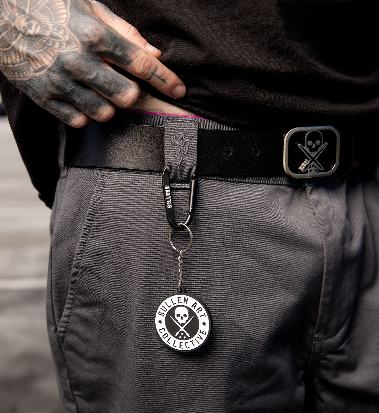 Person wearing a belt with a keychain featuring 'Sullen Art Collective' logo.