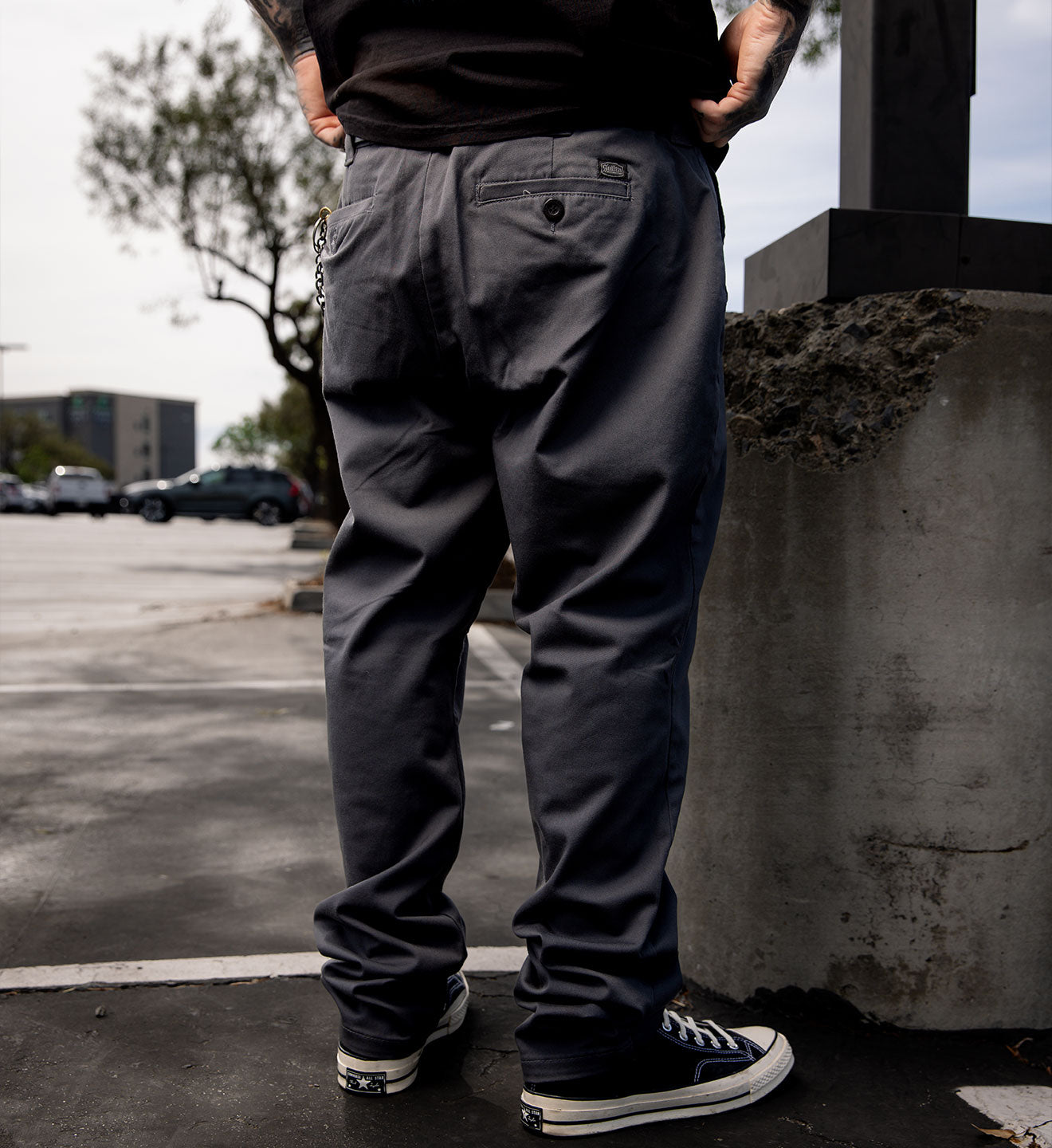 Person wearing dark gray cargo pants standing in an outdoor setting with a concrete block and trees in the background.