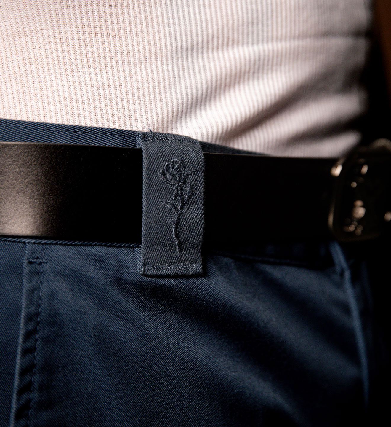 Close-up of a person wearing navy pants with a black belt and a visible brand logo.