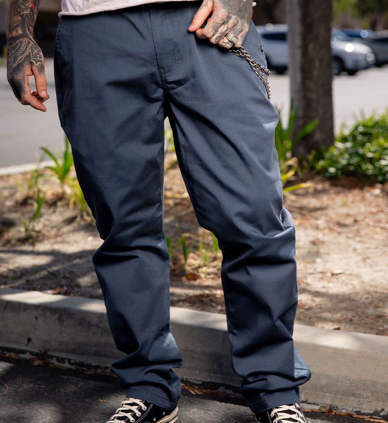 Person wearing dark blue pants standing on a sidewalk with a blurred background