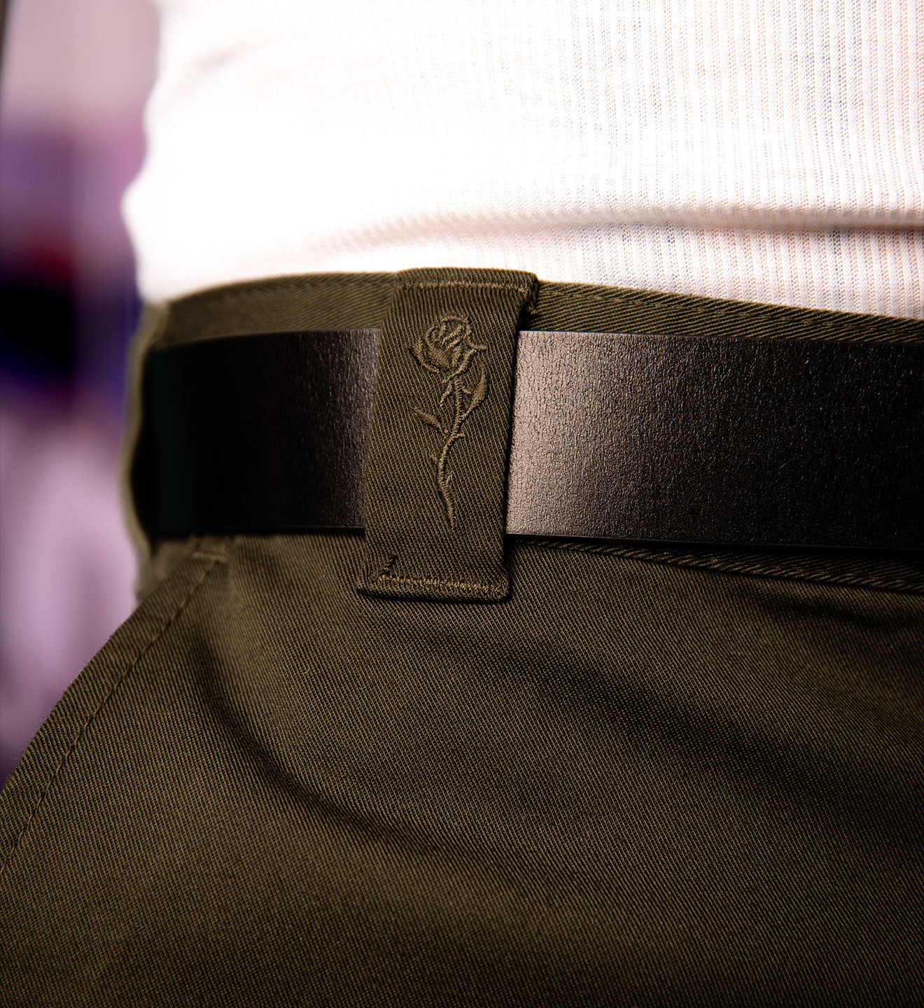 Close-up of a person wearing a black belt with a rose emblem on green pants against a blurred background.