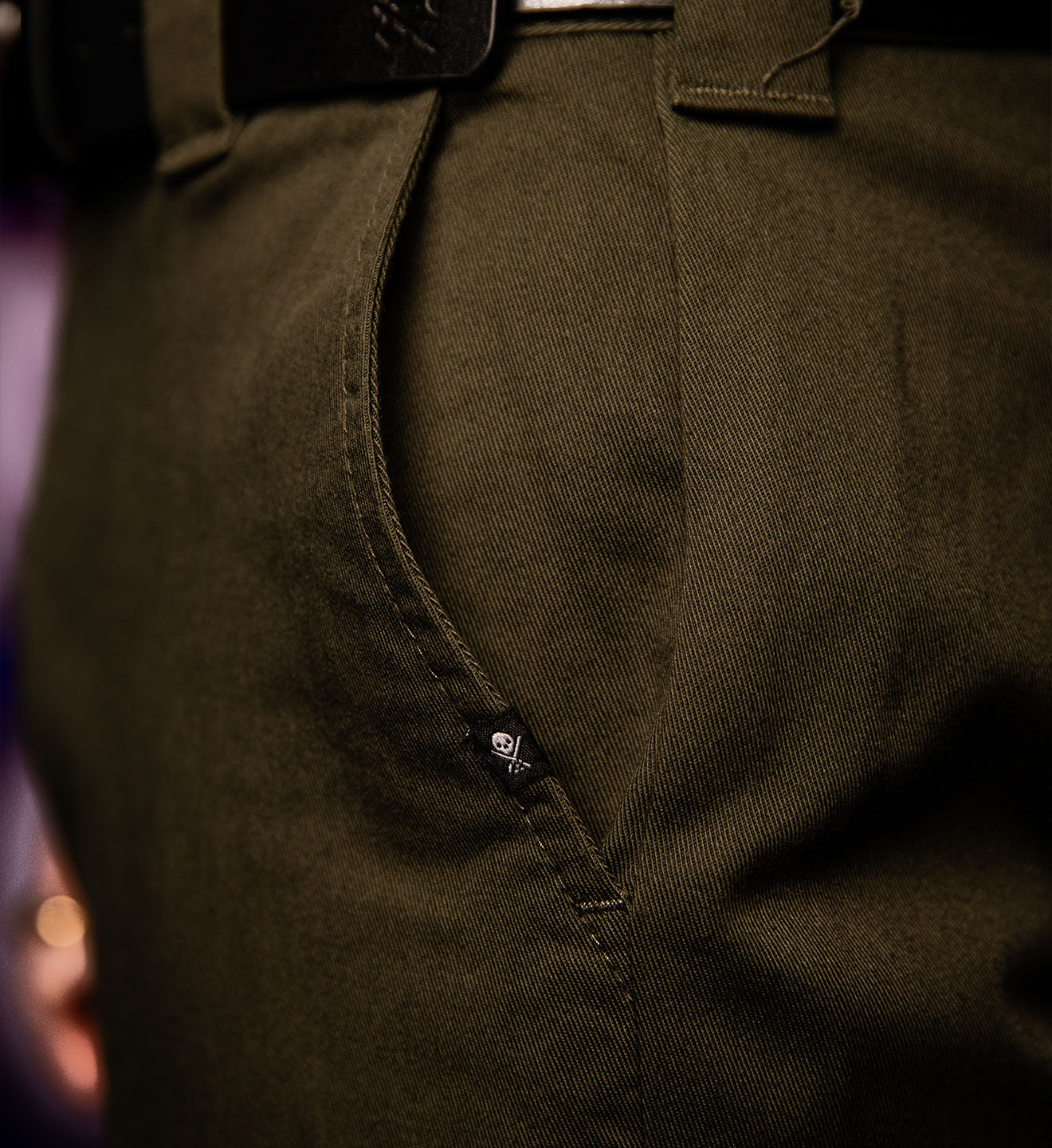 Close-up of dark green pants with a belt and button details.