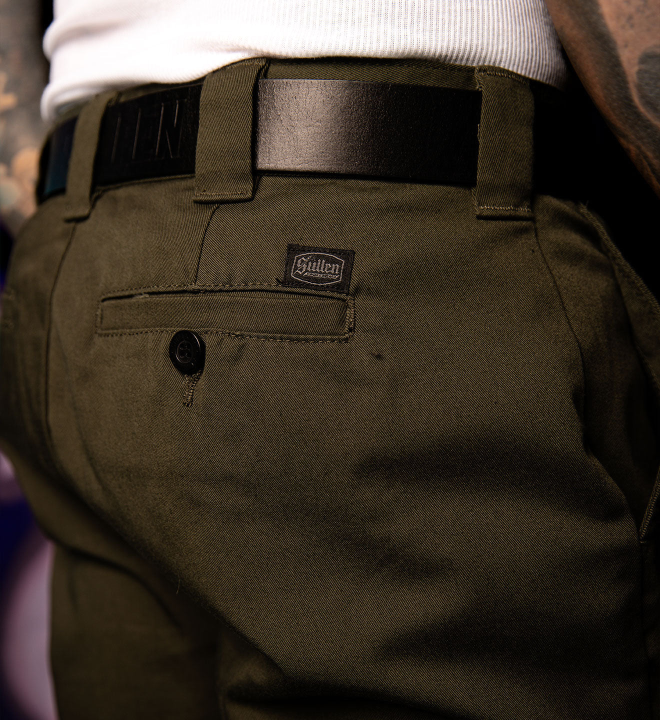 Close-up of a person wearing olive green pants with a brand label, blurred background