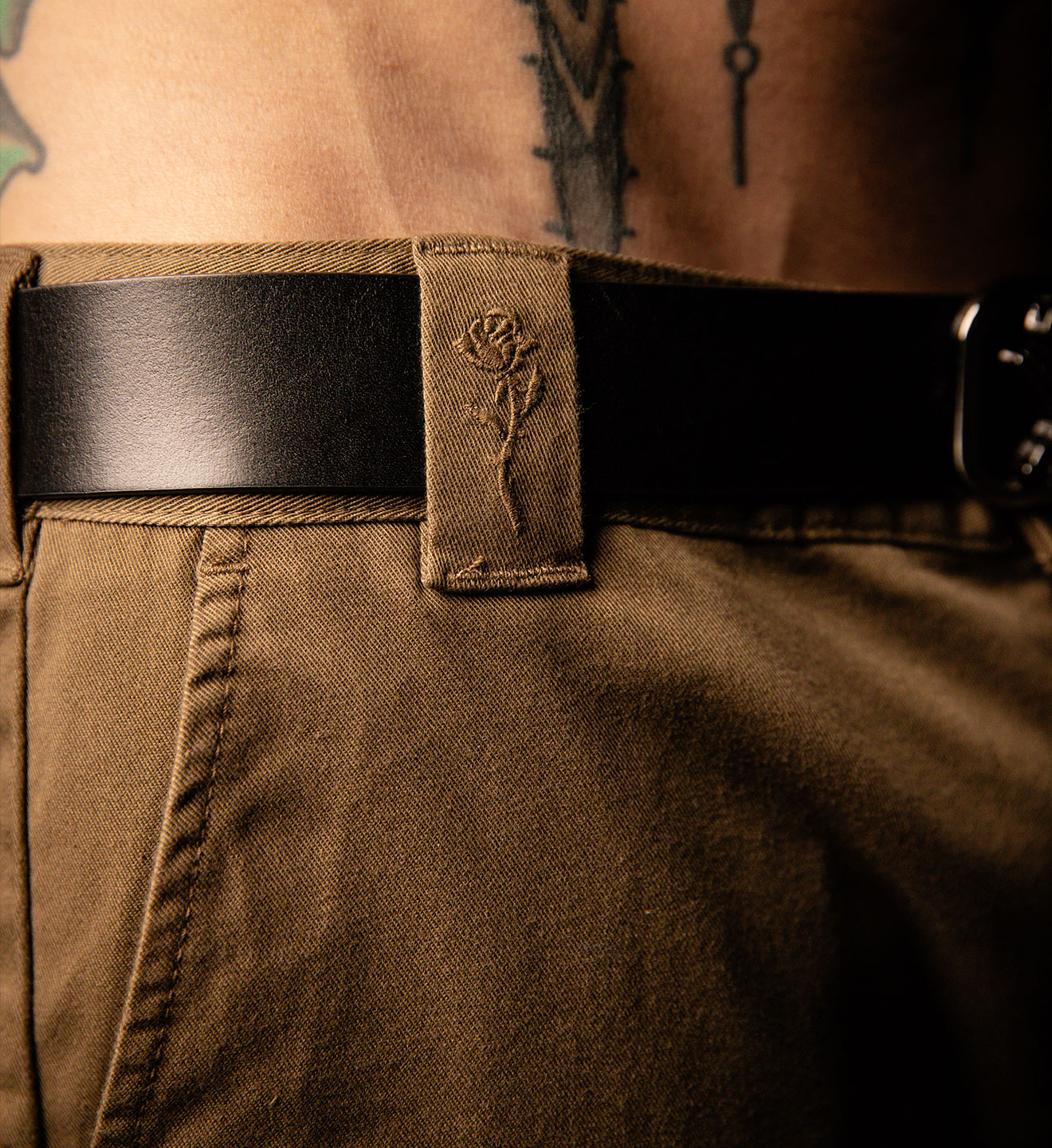 Brown leather belt with a rose emblem on a person wearing brown pants.