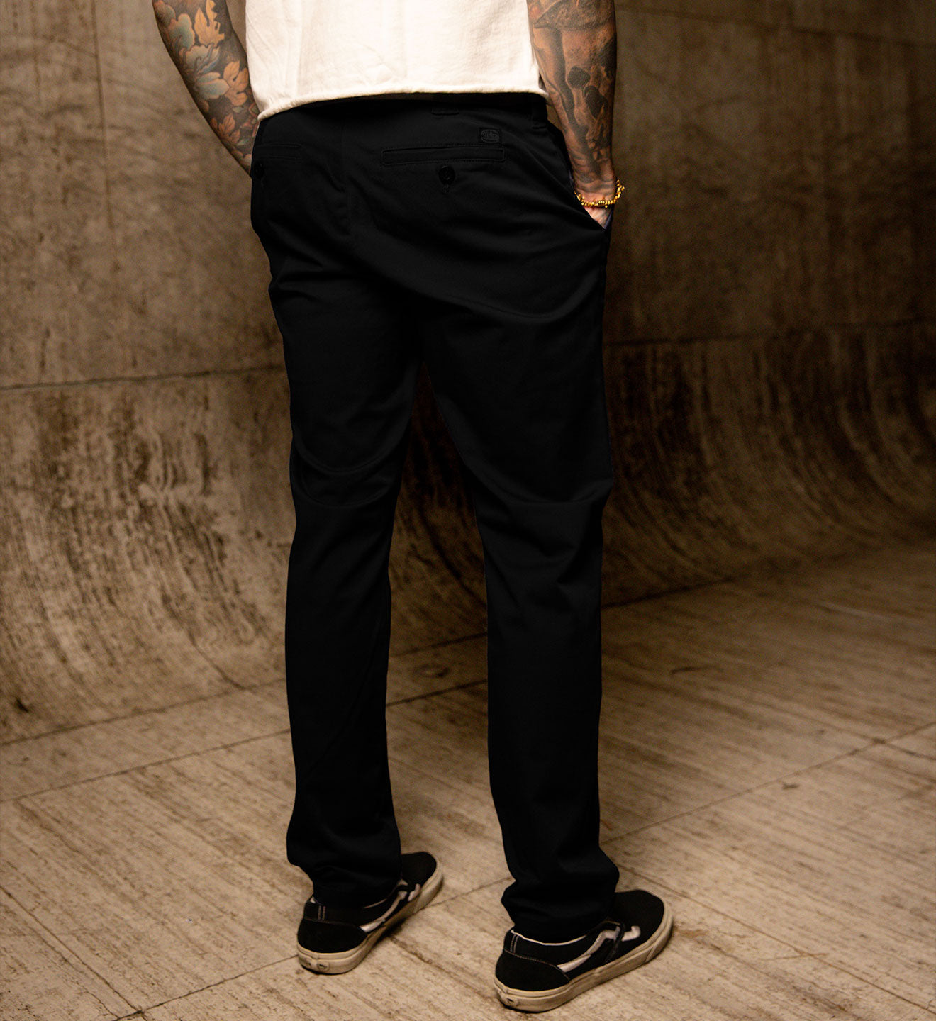 Person wearing black pants and a white shirt against a textured wall.