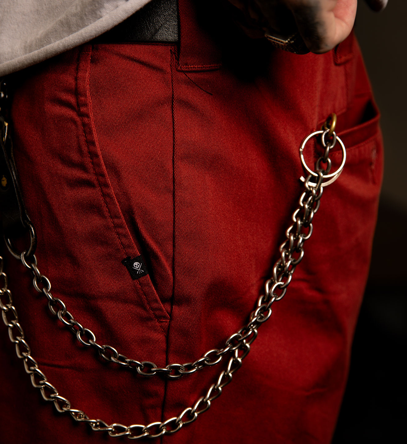 Person wearing red pants with a long chain hanging from the pocket against a dark background