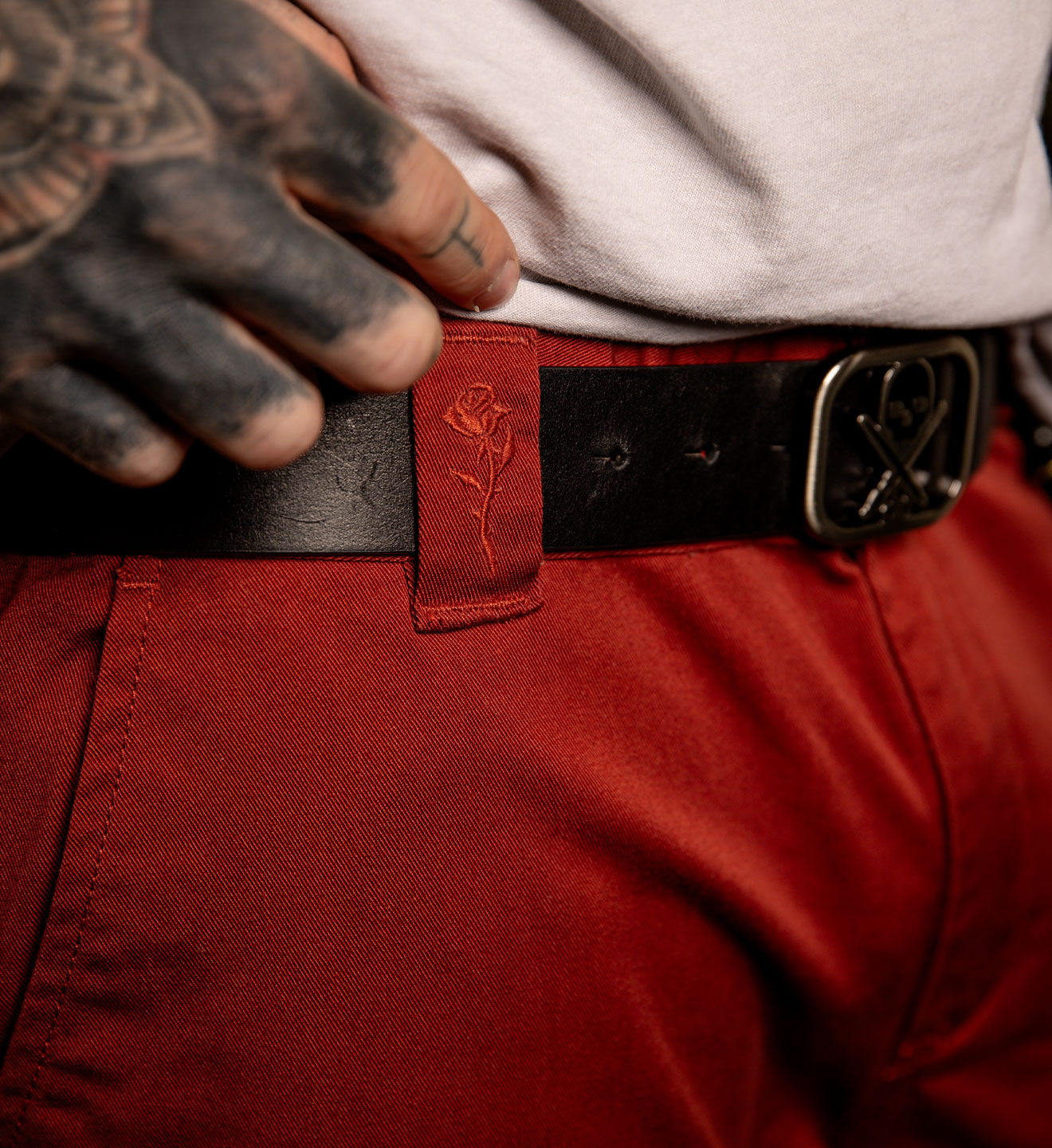 Person wearing a red belt with a rose emblem and a black belt buckle.