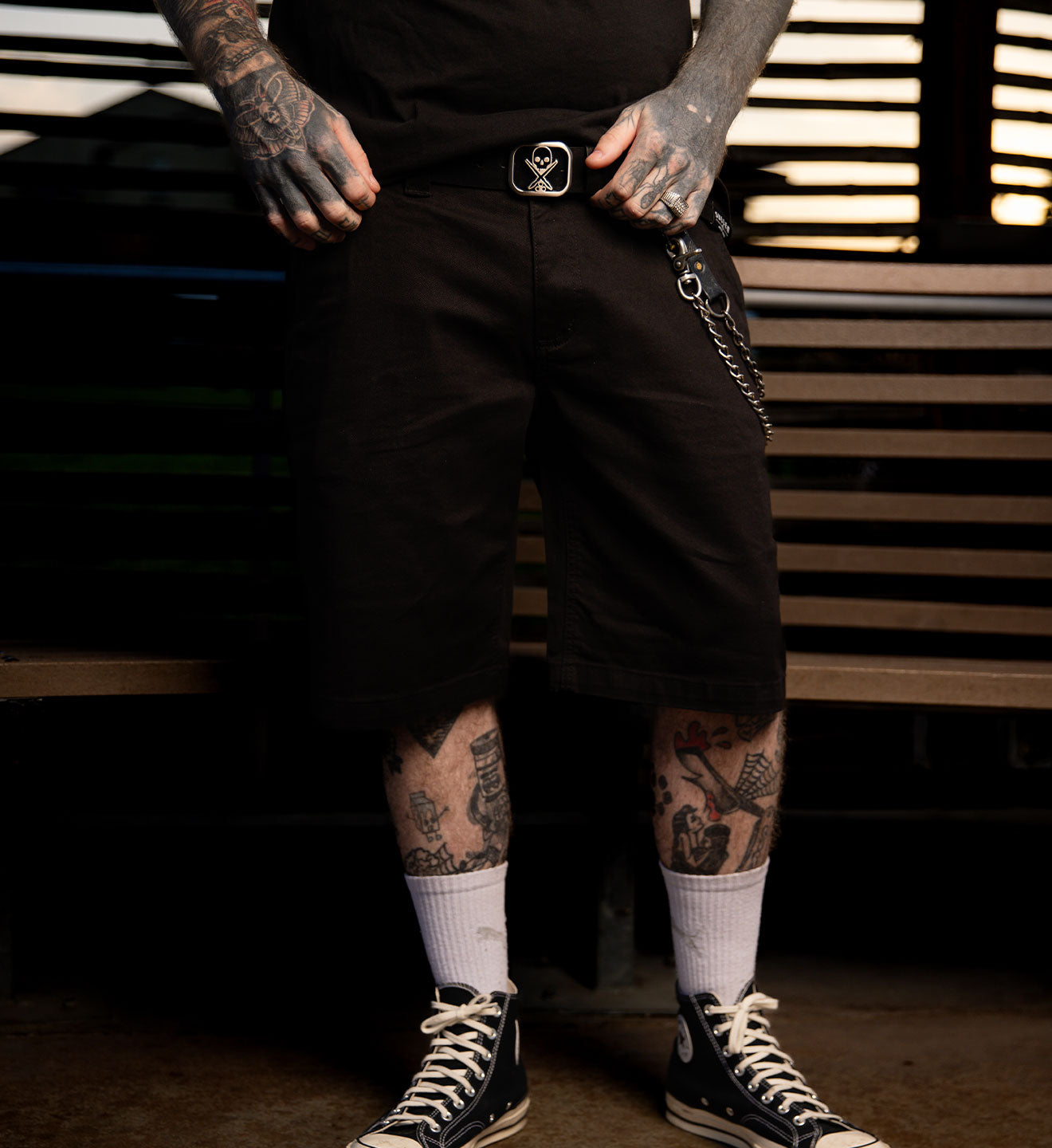 Person wearing black shorts with a belt and white socks, standing against a dark background.