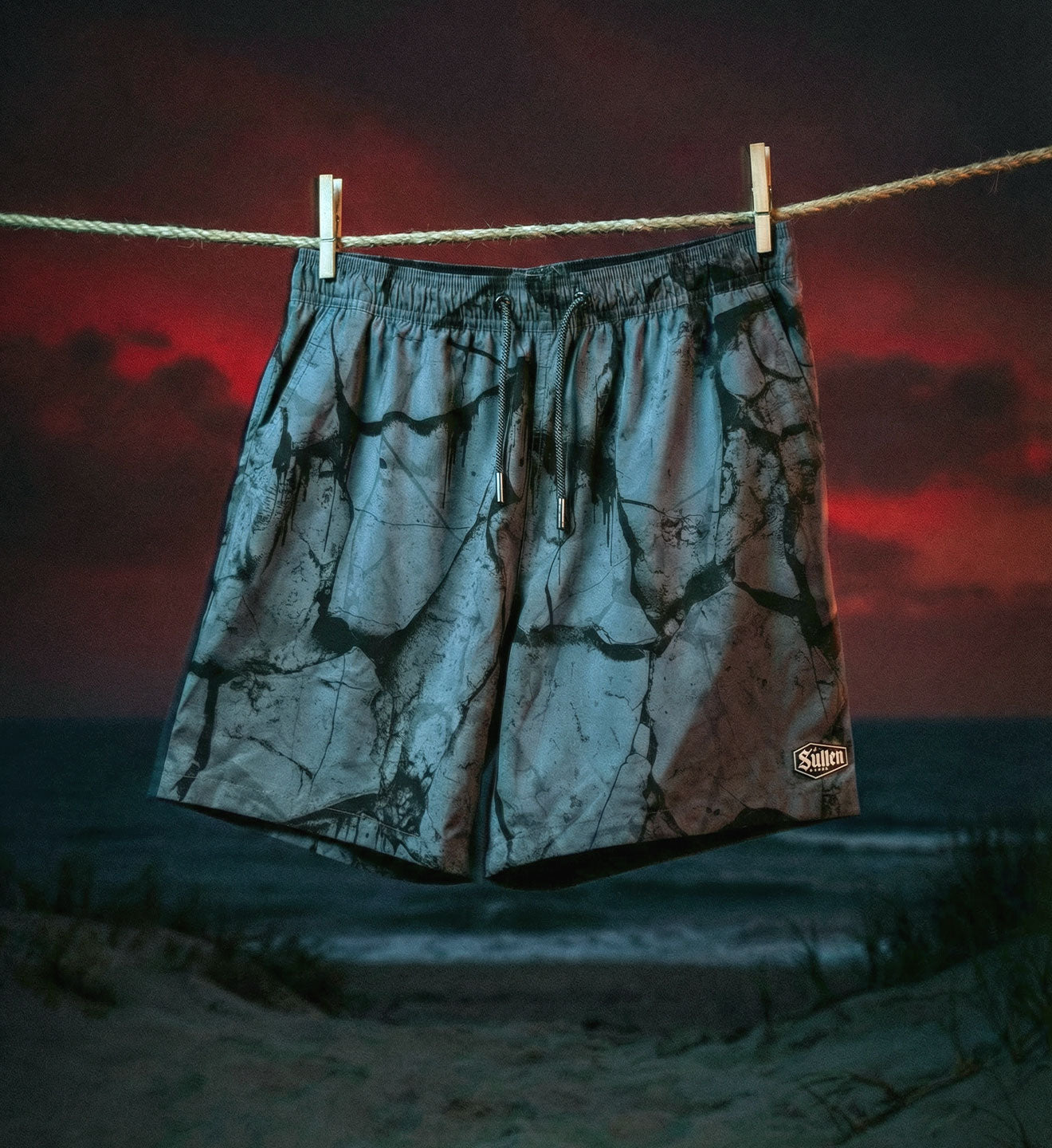 Camouflage shorts hanging on a clothesline with a sunset sky and ocean background
