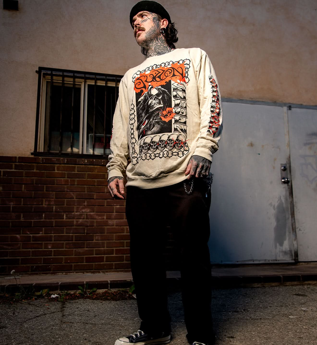 Man wearing a graphic sweatshirt standing against a wall with a door.