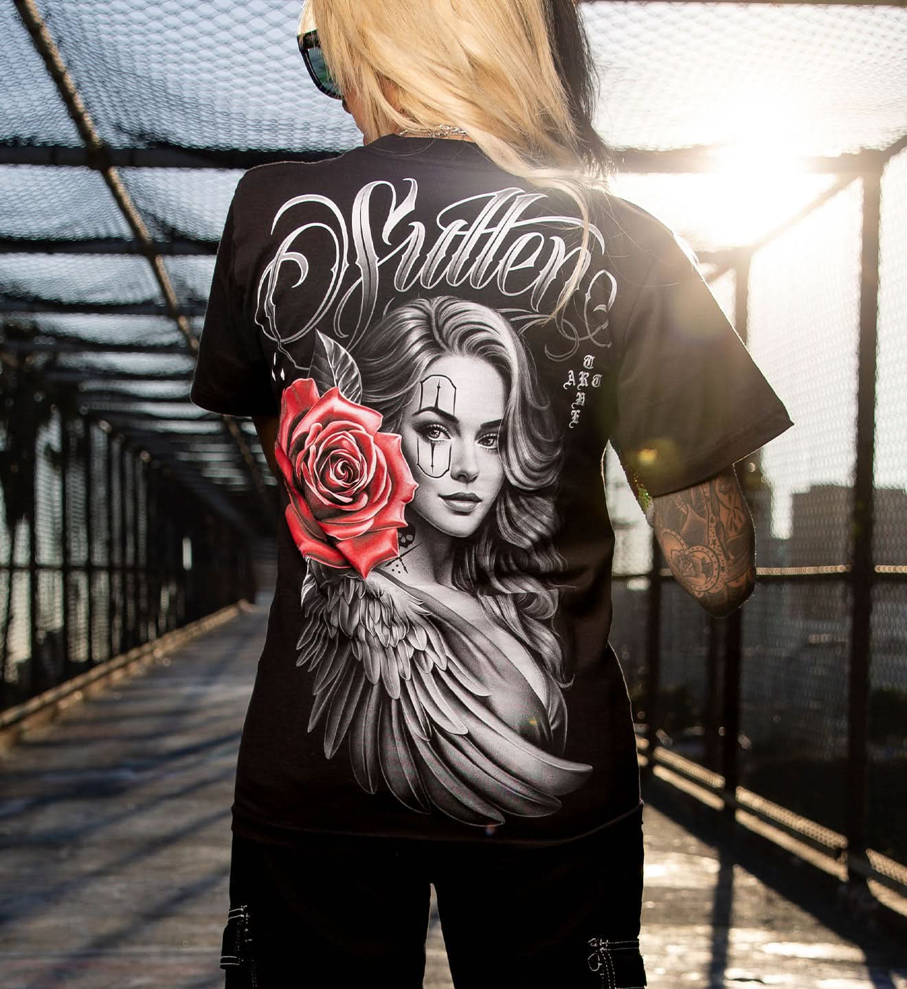 Person wearing a black t-shirt with a graphic design of a woman's face, red rose, and 'Strether' text.