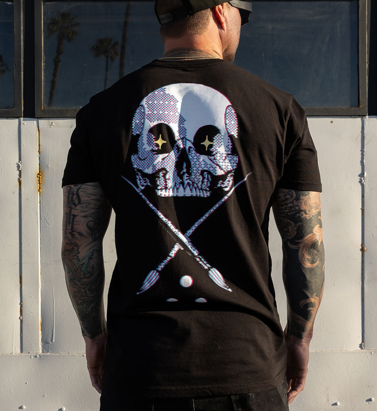 Person wearing a black t-shirt with a graphic design on the back, standing against a white wall.