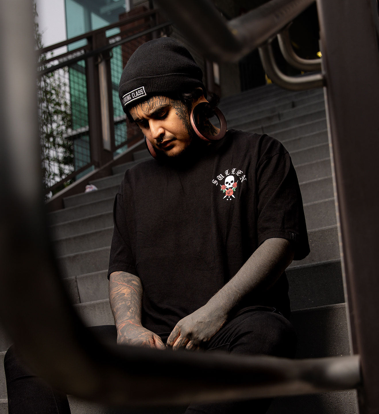 Person wearing a black t-shirt with a skull design, sitting on steps.