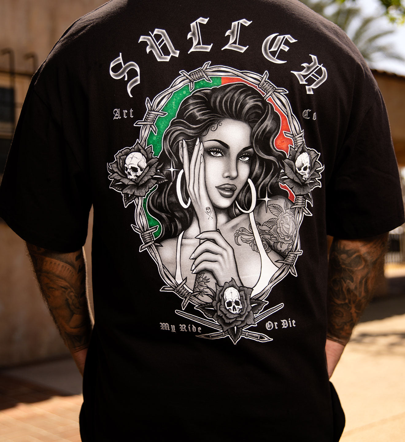 Person wearing a black t-shirt with a graphic design on the back, standing outdoors.