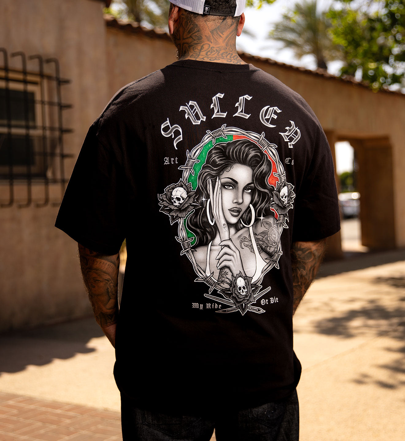 Person wearing a black t-shirt with a graphic design on the back, standing outdoors.