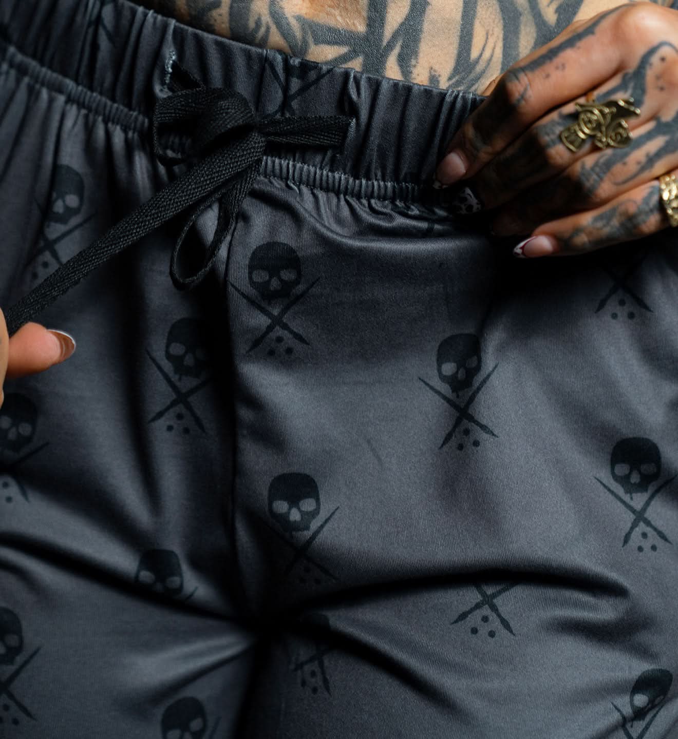 Black pants with skull and crossbones pattern worn by a person with tattoos.