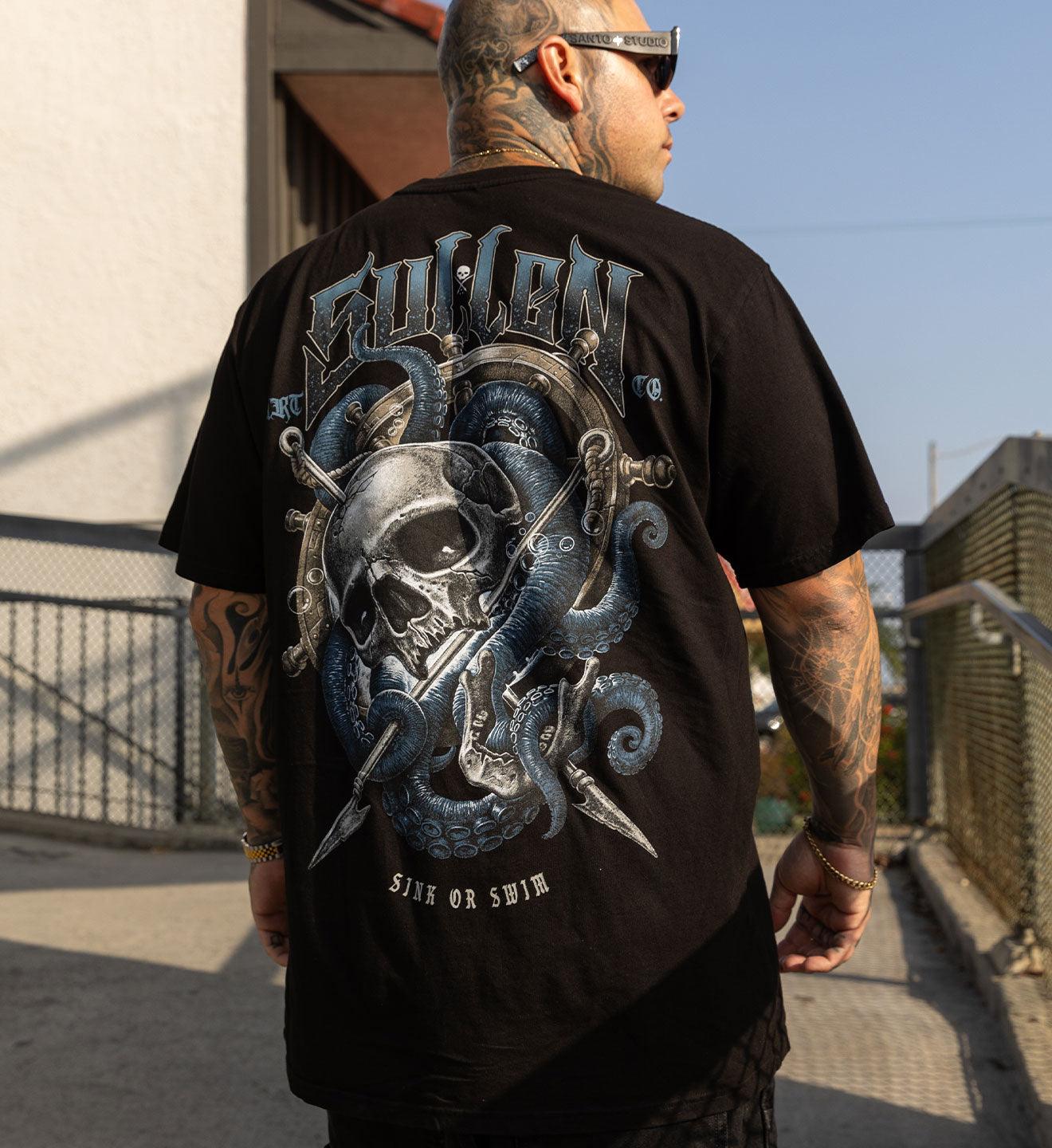 Man wearing a black t-shirt with a graphic design on the back, standing outdoors.