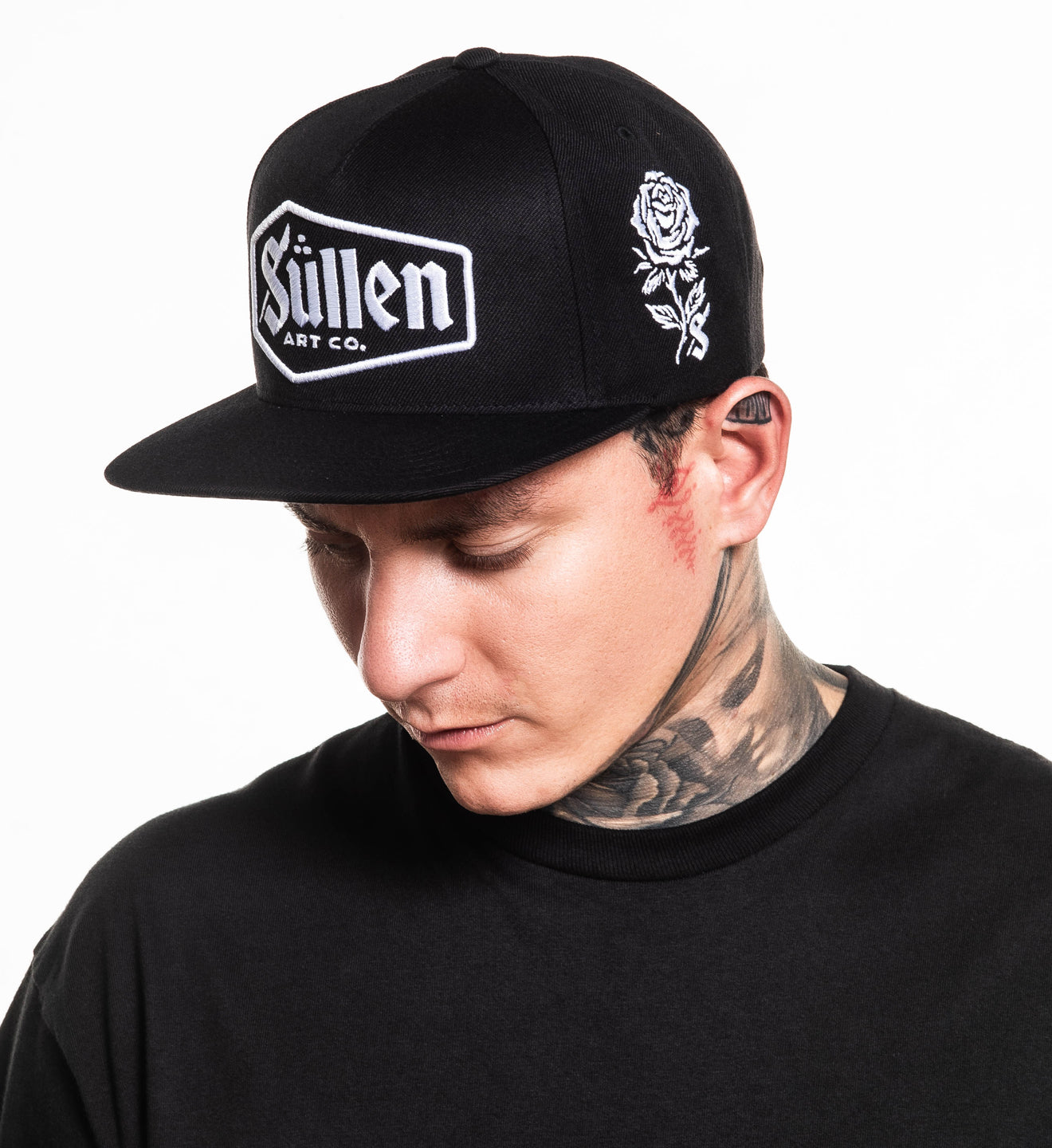 Person wearing a black cap with 'Sullen' logo and rose design on a white background