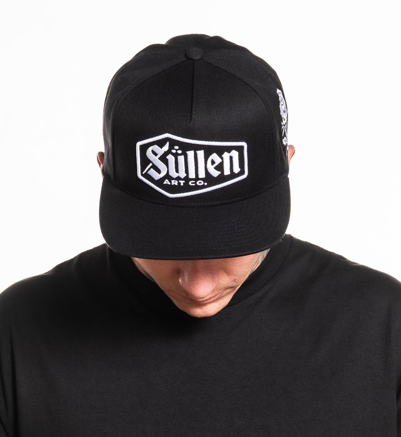 Person wearing a black cap with 'Sullen Art Co.' logo on a white background