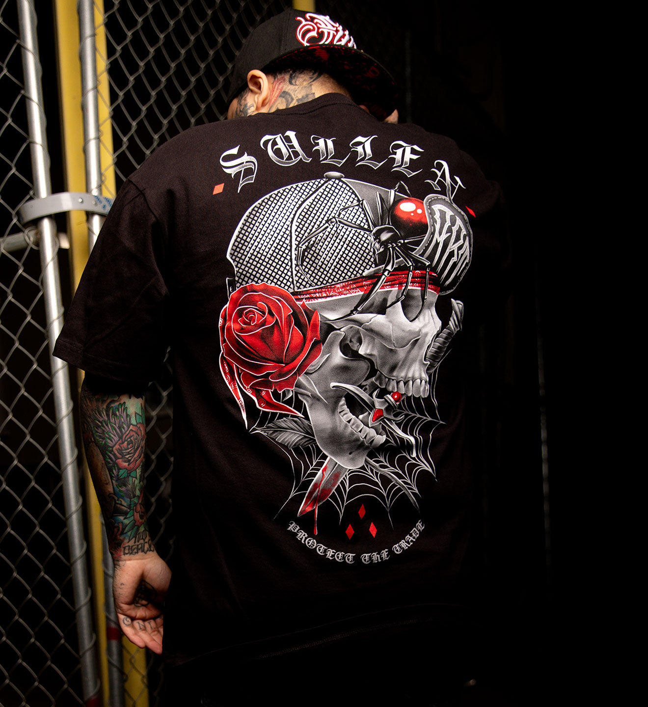 Person wearing a black t-shirt with a skull and rose design, standing against a dark background.