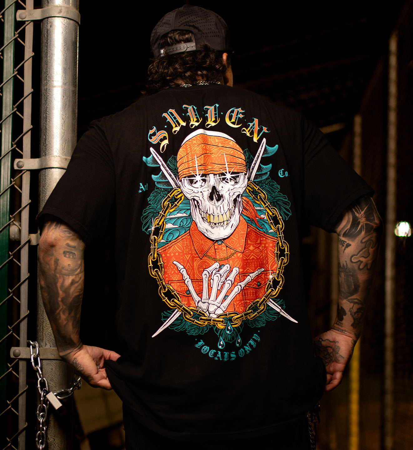 Person wearing a black t-shirt with a colorful graphic design on the back, standing against a dark background.