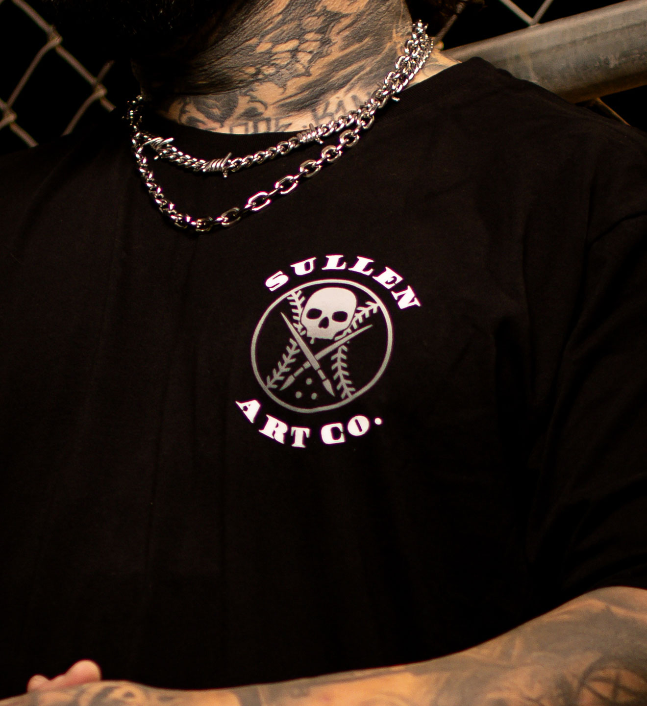 Black t-shirt with 'Sullen Art Co.' logo worn by a person with tattoos.
