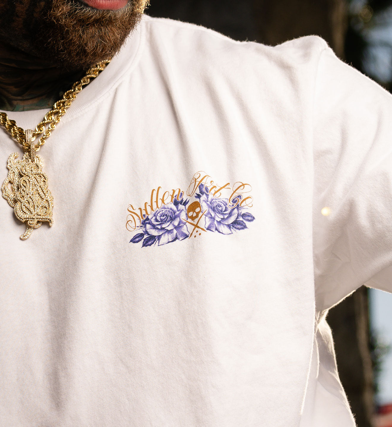 White t-shirt with floral design and text, worn by a person with a gold chain.