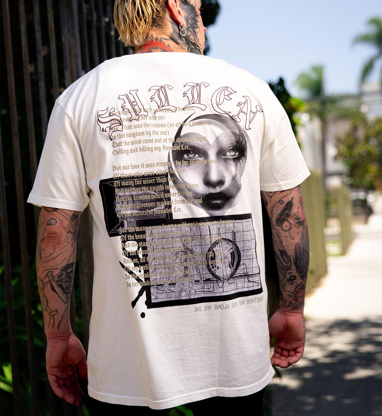 Person wearing a white t-shirt with graphic design and text, standing outdoors.