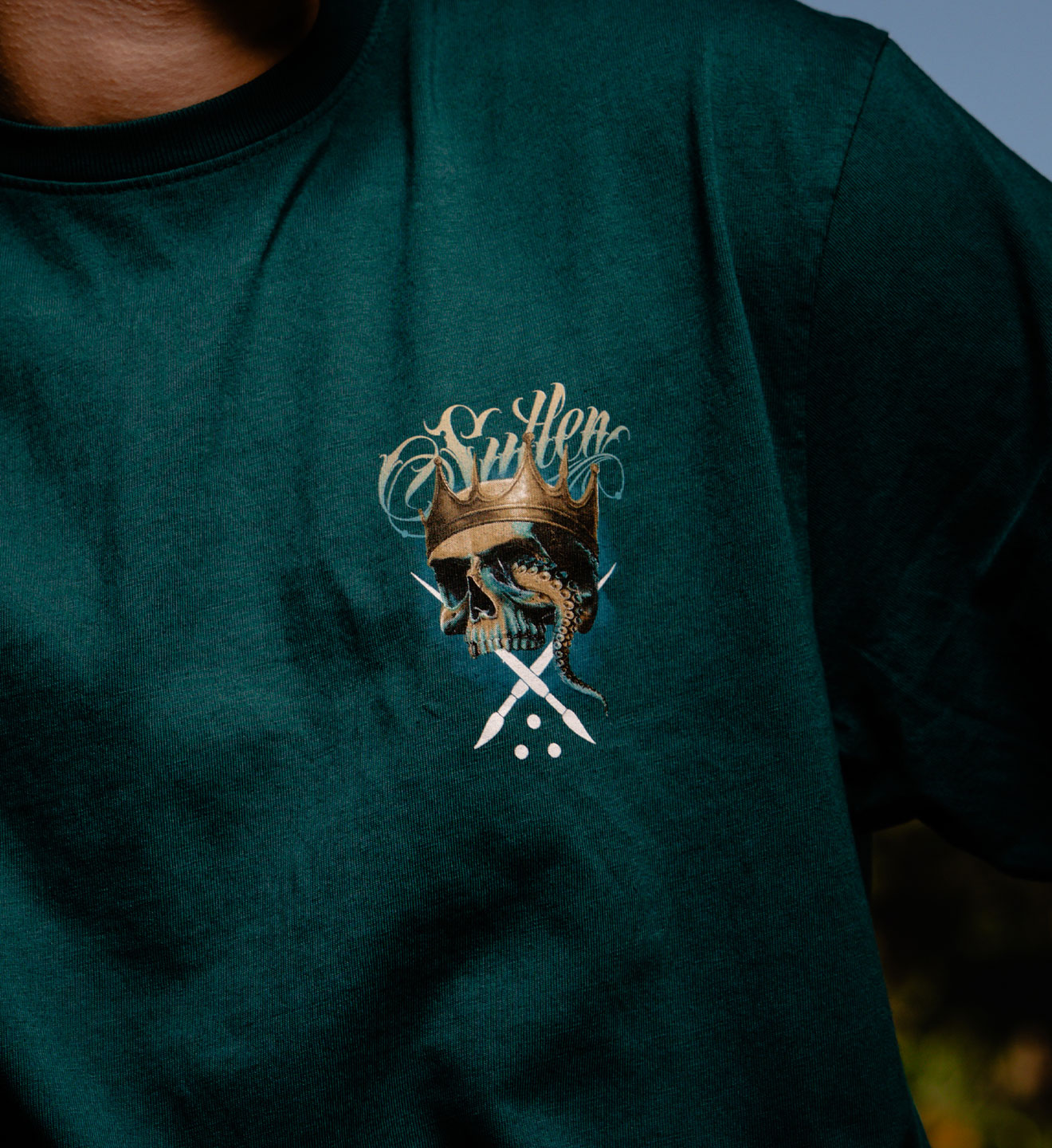 Green t-shirt with a skull and crown design on a person wearing it.