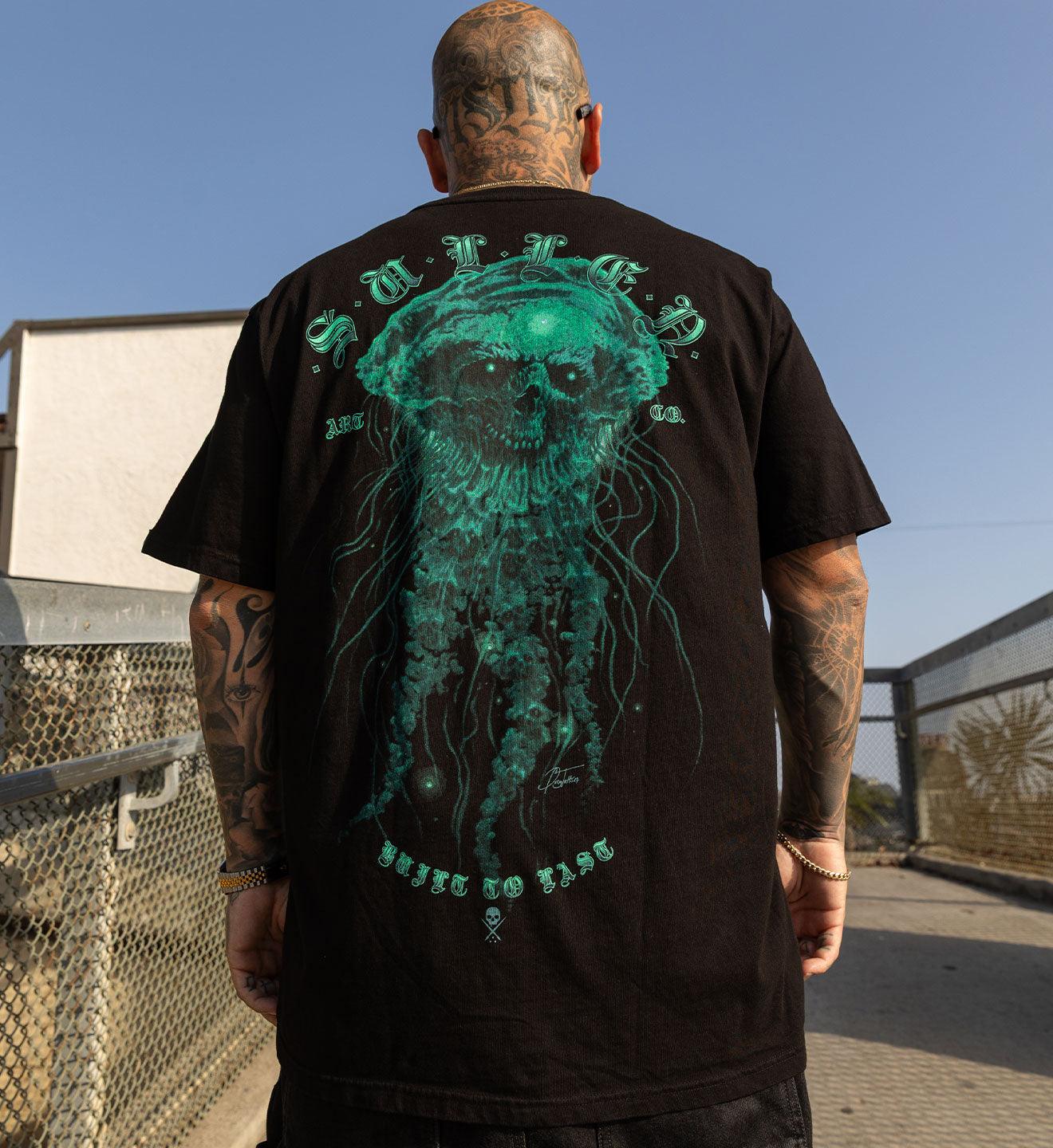 Person wearing a black t-shirt with a green jellyfish design on the back, standing outdoors.