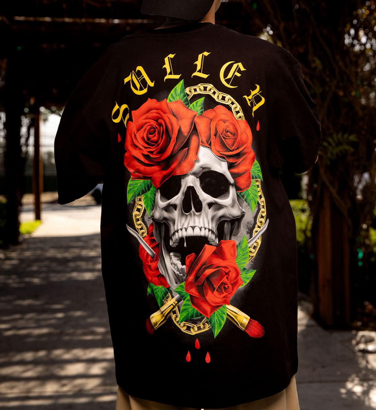 Black t-shirt with a skull and roses design on the back, worn by a person outdoors.