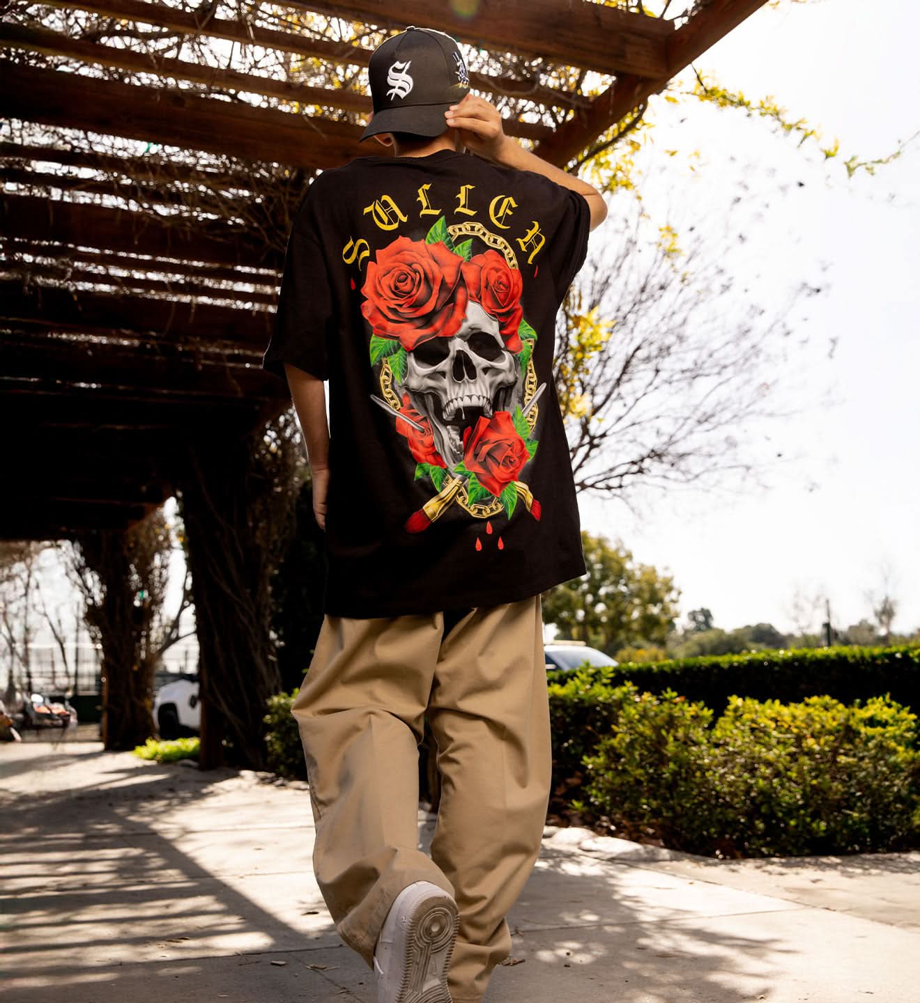 Person wearing a black t-shirt with a skull and roses design, walking outdoors.