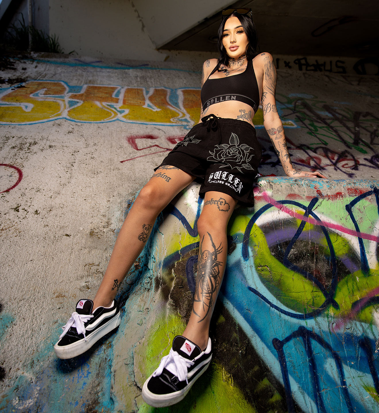 Person sitting on a graffiti-covered wall wearing black sneakers and shorts.