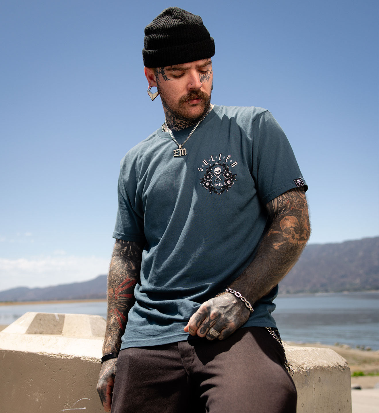 Man wearing a blue t-shirt with a logo, sitting by a body of water.