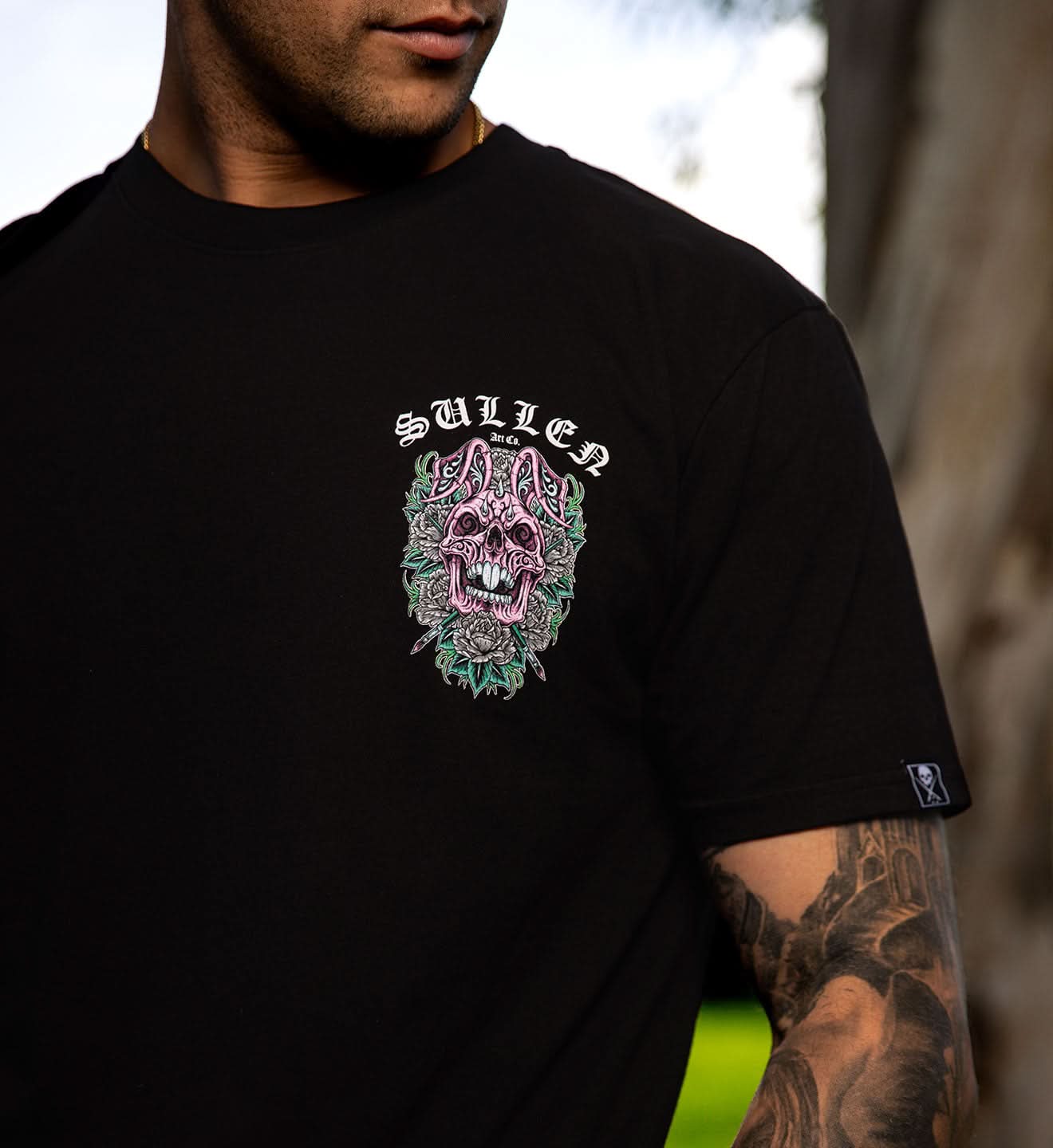 Person wearing a black t-shirt with a colorful graphic design and 'Sullen' branding.
