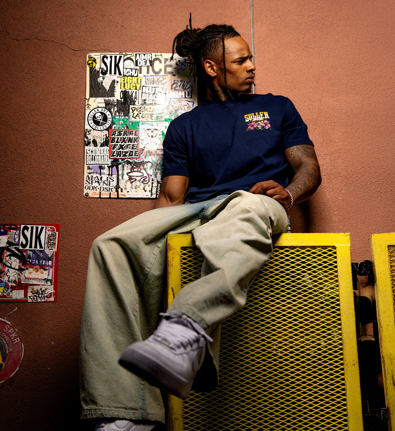 Person sitting on a yellow metal box against a brown wall with posters.