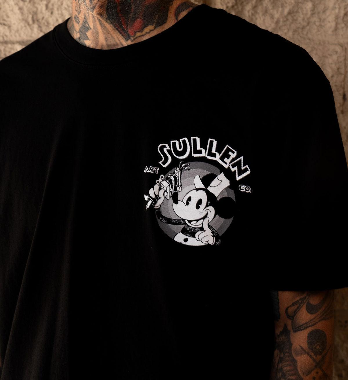 Black t-shirt with a graphic design and 'Sullen' branding on a textured wall background.