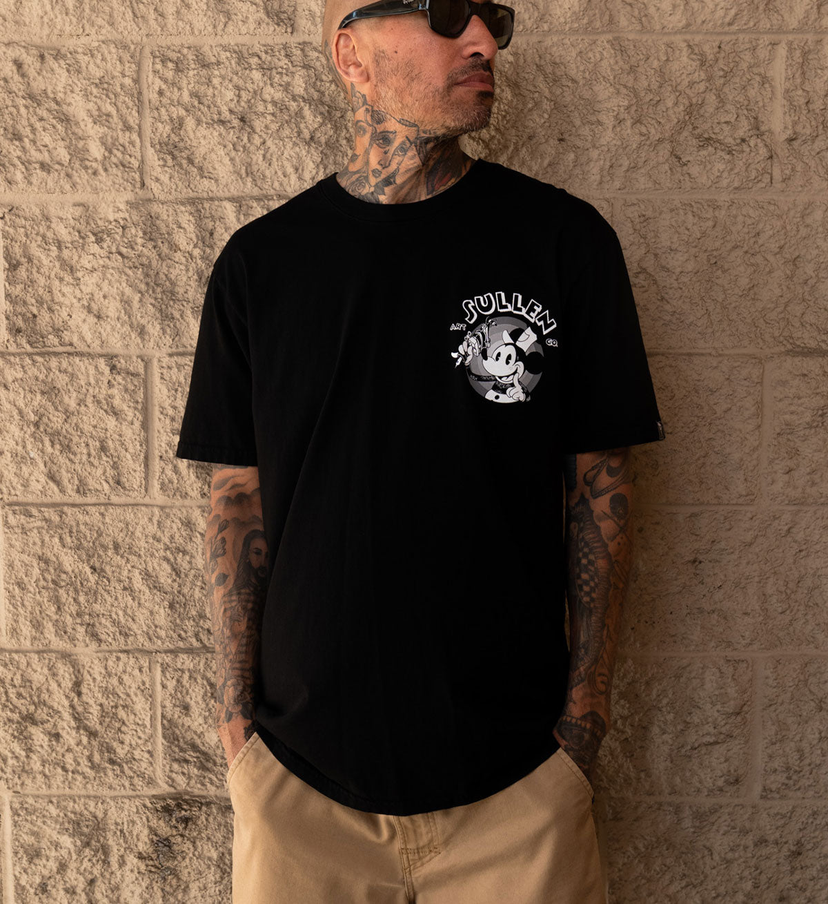 Man wearing a black t-shirt with a graphic design against a textured wall.