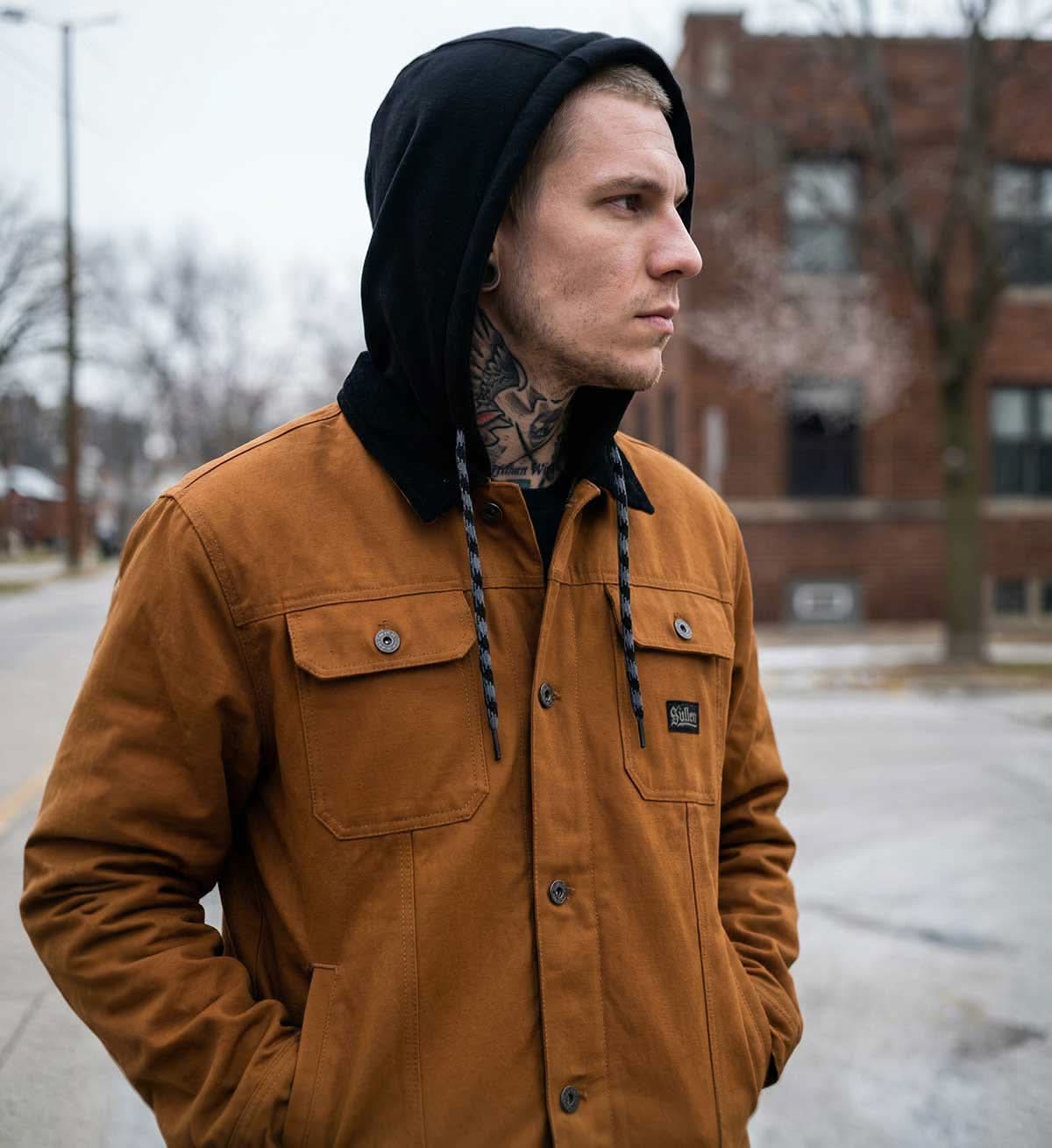 Man wearing a brown jacket and black beanie standing on a street.