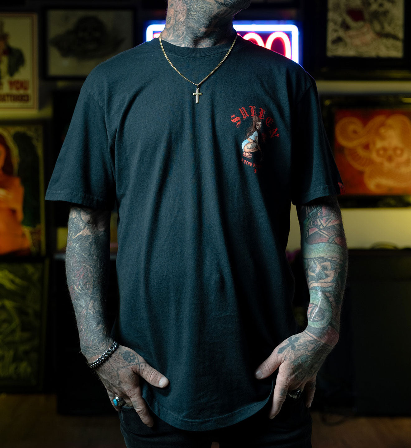 Person wearing a black t-shirt with a logo, standing in a room with posters and neon signs.