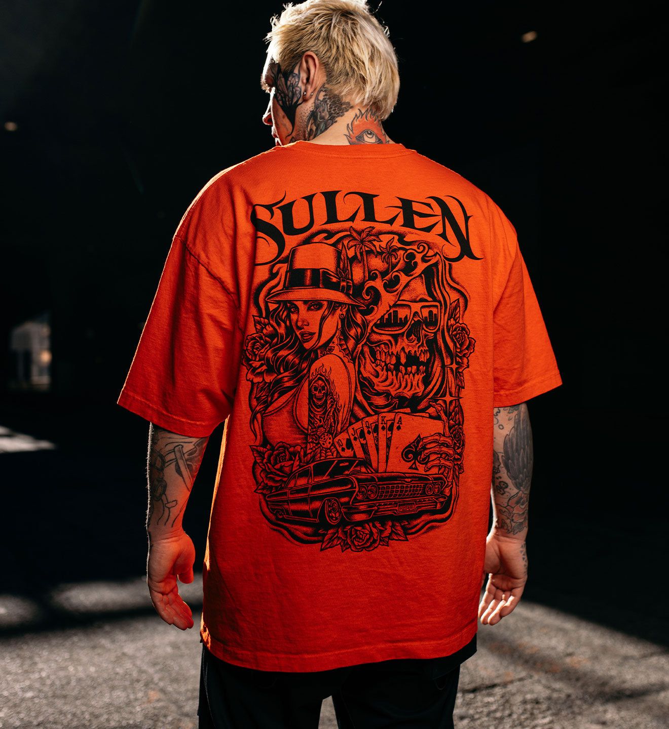 Person wearing a red 'Sullen' t-shirt with a graphic design on the back, standing in a dark setting.