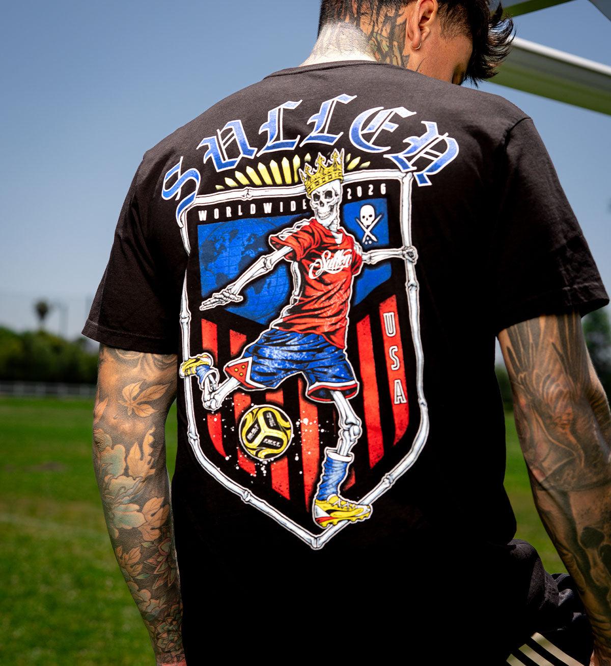 Person wearing a black t-shirt with a colorful graphic design on the back, featuring a skeleton playing soccer.